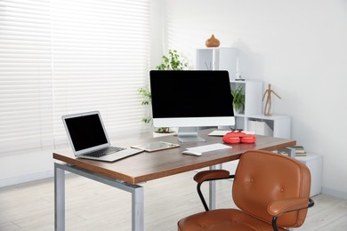 Photo of Modern workplace with computer, laptop, tablet and headphones on wooden desk in office