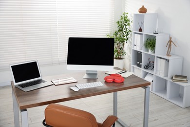 Photo of Modern workplace with computer, laptop, tablet and headphones on wooden desk in office