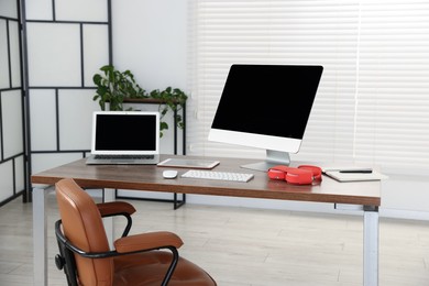 Photo of Modern workplace with computer, laptop, tablet and headphones on wooden desk in office