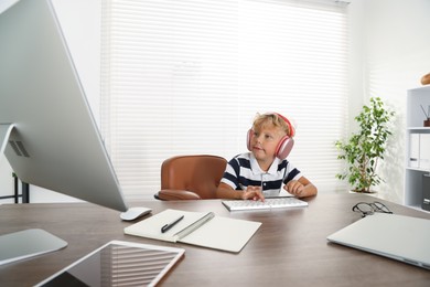 Photo of Choice of profession. Little boy with headphones pretending to work on computer in office