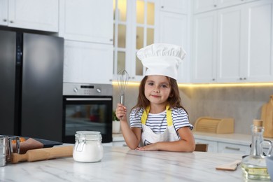 Photo of Choice of profession. Little girl with whisk pretending to be chef in kitchen