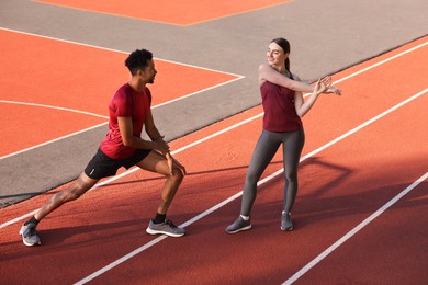 Photo of Couple in sportswear doing warm-up exercises before run at stadium