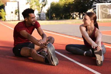 Photo of Smiling couple in sportswear stretching before run at stadium
