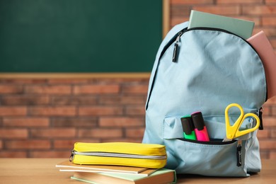 Photo of Light blue backpack with different stationery, pencil case and book on desk in classroom, closeup. Space for text
