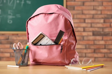 Photo of Pink backpack with different stationery on desk in classroom