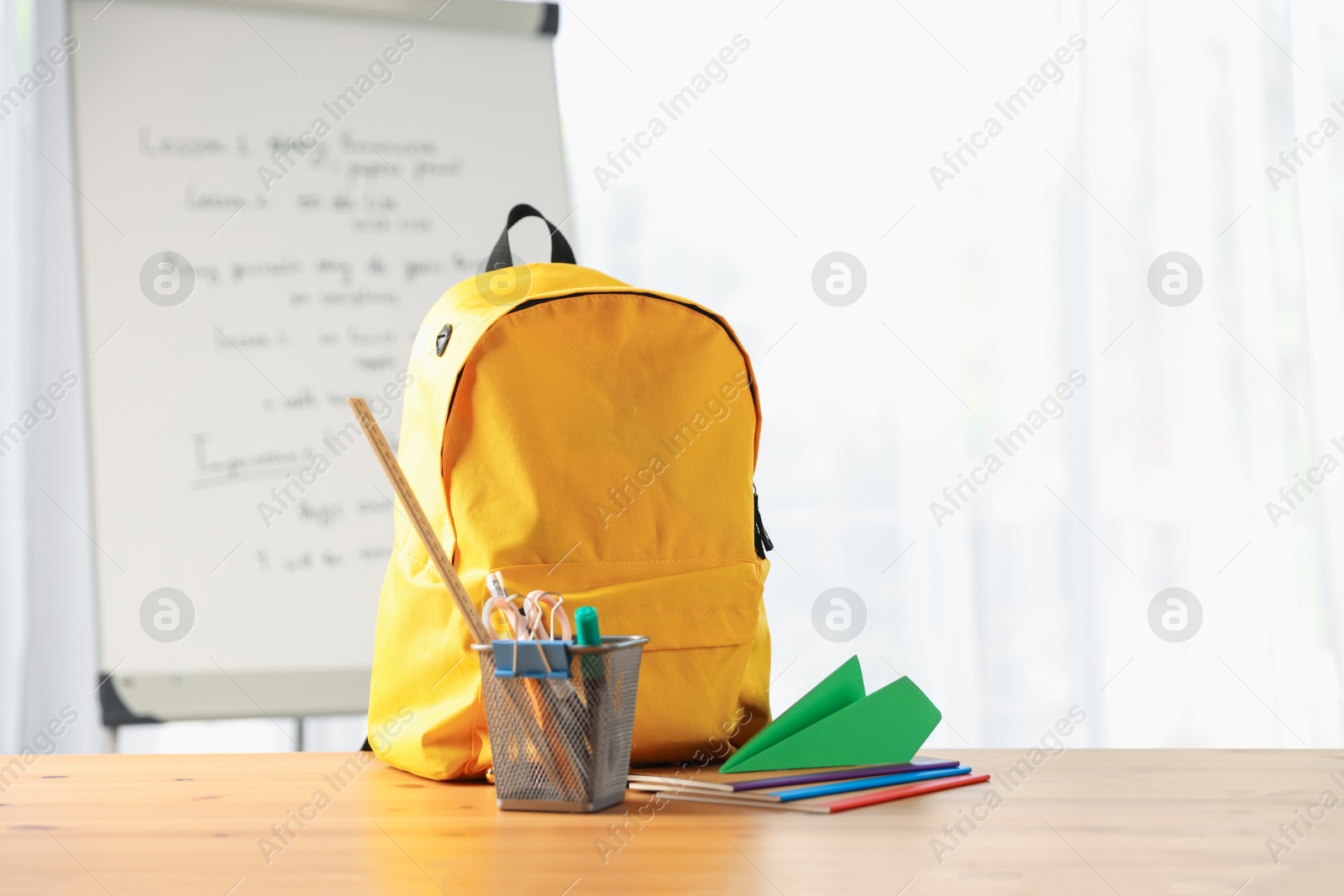 Photo of Backpack, different stationery and paper plane on desk in classroom