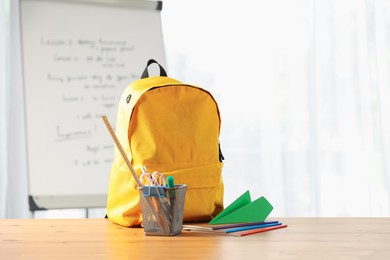 Photo of Backpack, different stationery and paper plane on desk in classroom