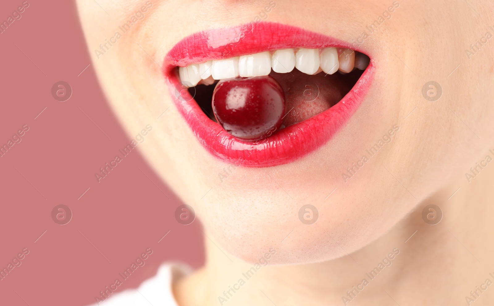 Woman with beautiful lips makeup and cherry on dusty pink background, closeup Photo of Woman with beautiful lips makeup and cherry on dusty pink background, closeup