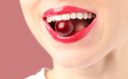 Photo of Woman with beautiful lips makeup and cherry on dusty pink background, closeup