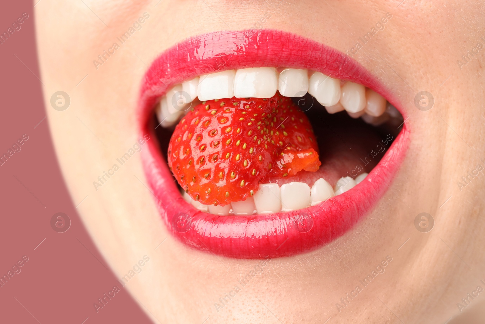 Woman with beautiful lips makeup and strawberry on dusty pink background, closeup Photo of Woman with beautiful lips makeup and strawberry on dusty pink background, closeup