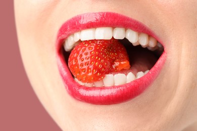 Photo of Woman with beautiful lips makeup and strawberry on dusty pink background, closeup