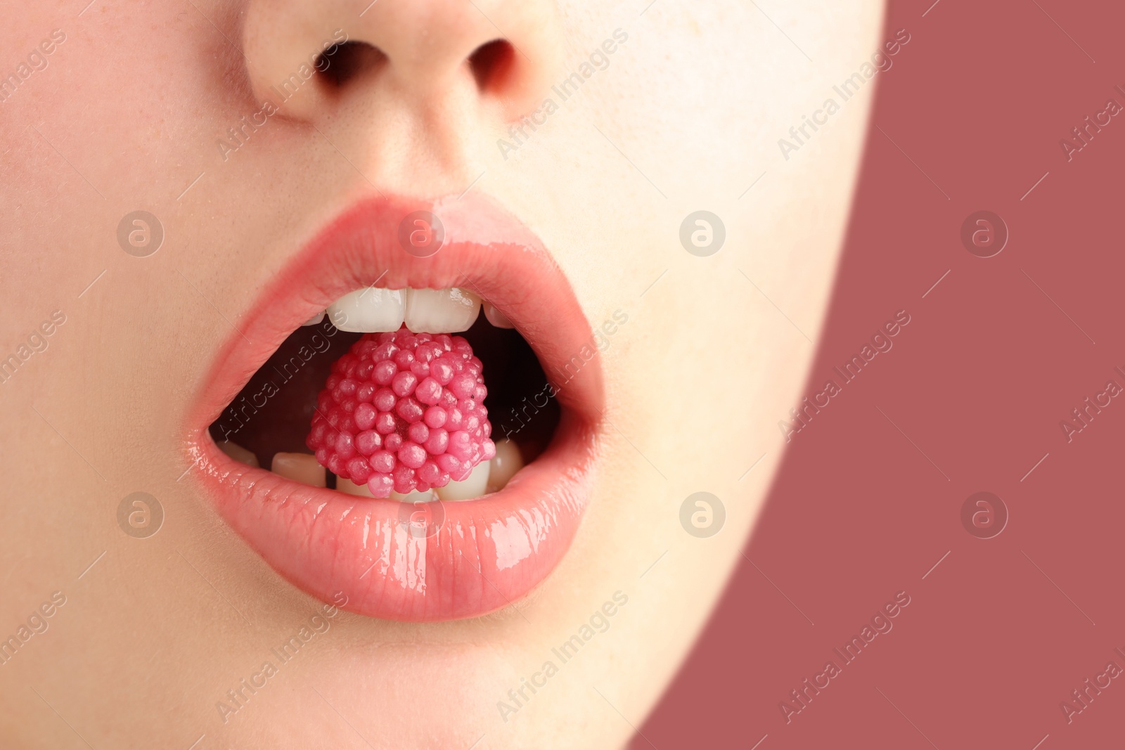 Woman with beautiful lips makeup and raspberry candy on dusty pink background, closeup. Space for text Photo of Woman with beautiful lips makeup and raspberry candy on dusty pink background, closeup. Space for text
