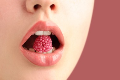 Photo of Woman with beautiful lips makeup and raspberry candy on dusty pink background, closeup. Space for text