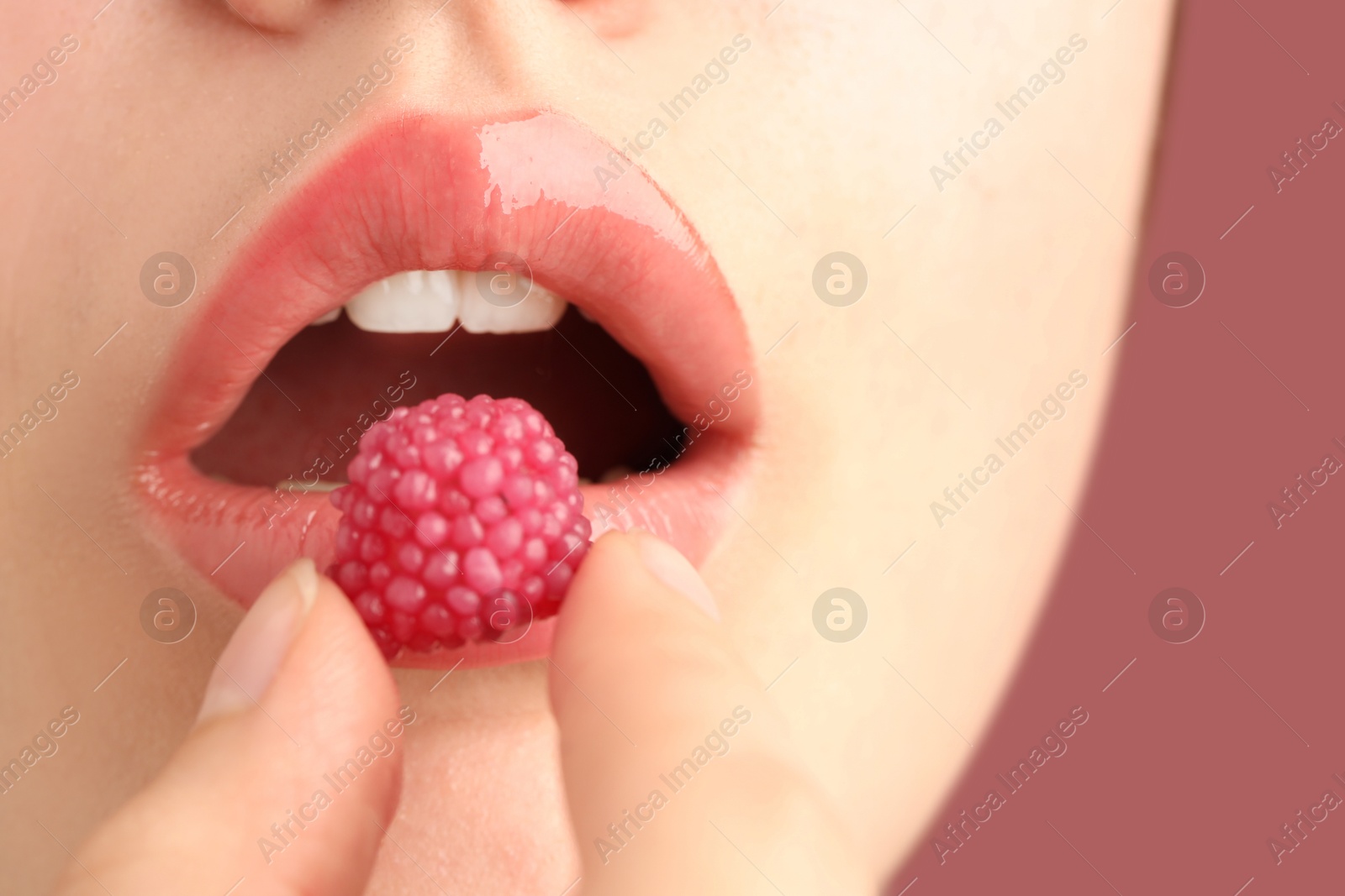 Woman with beautiful lips makeup and raspberry candy on dusty pink background, closeup Photo of Woman with beautiful lips makeup and raspberry candy on dusty pink background, closeup