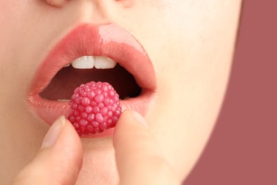 Photo of Woman with beautiful lips makeup and raspberry candy on dusty pink background, closeup