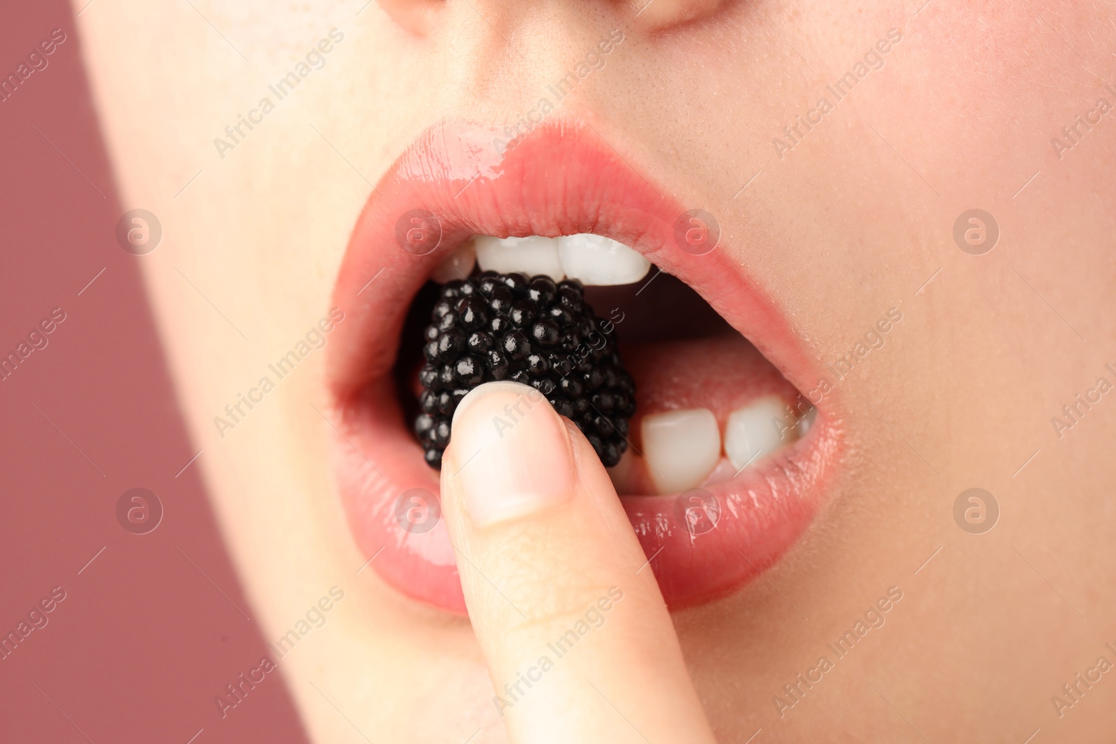 Woman with beautiful lips makeup and blackberry on dusty pink background, closeup Photo of Woman with beautiful lips makeup and blackberry on dusty pink background, closeup