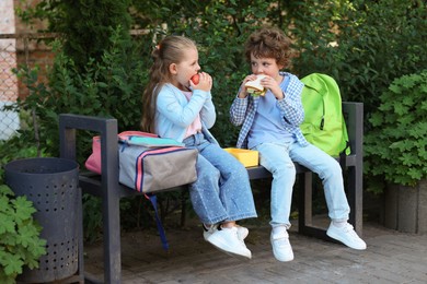 Photo of Cute kids eating food on bench outdoors. School lunch