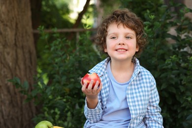 Photo of Cute little boy eating apple outdoors, space for text. School lunch