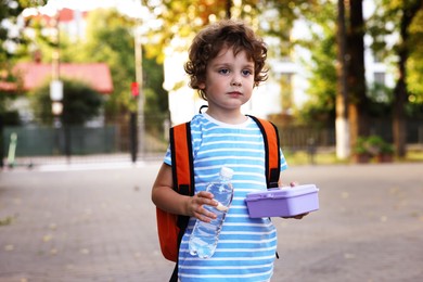 Photo of Cute little boy with school lunch box and bottle of water outdoors