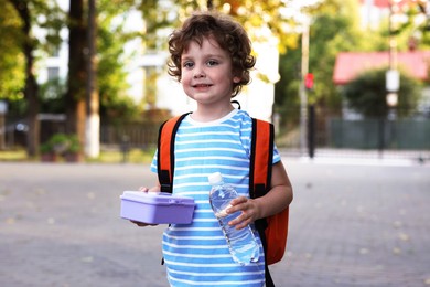 Photo of Cute little boy with school lunch box and bottle of water outdoors