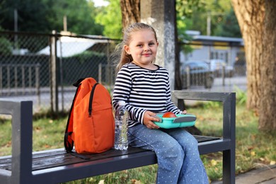 Photo of Cute little boy with school lunch box on bench outdoors