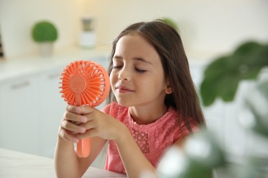 Photo of Little girl enjoying air flow from portable fan at home. Summer heat