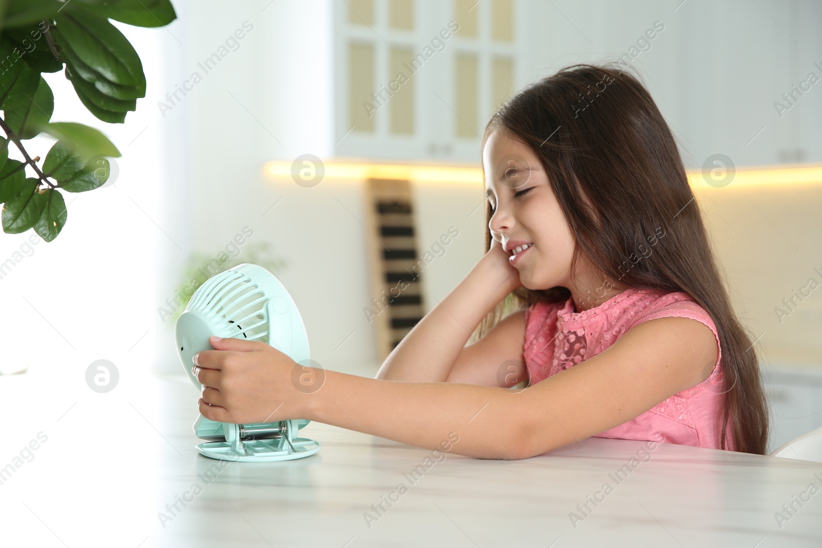 Photo of Little girl enjoying air flow from portable fan at home. Summer heat