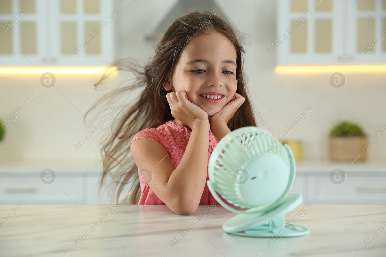 Photo of Little girl enjoying air flow from portable fan at home. Summer heat