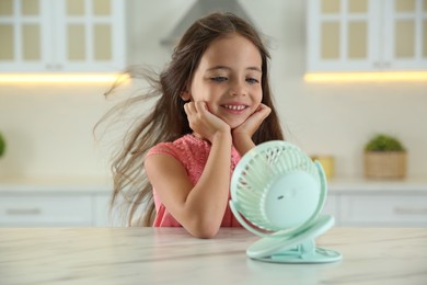 Photo of Little girl enjoying air flow from portable fan at home. Summer heat