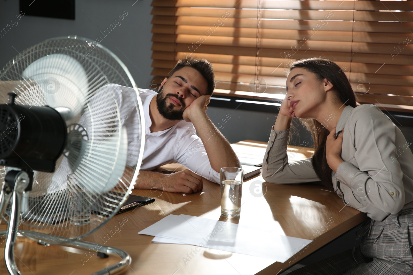 Photo of Office employees sitting in front of fan at workplace. Summer heat