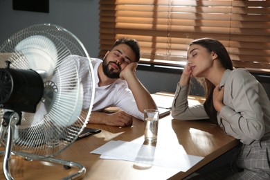 Photo of Office employees sitting in front of fan at workplace. Summer heat
