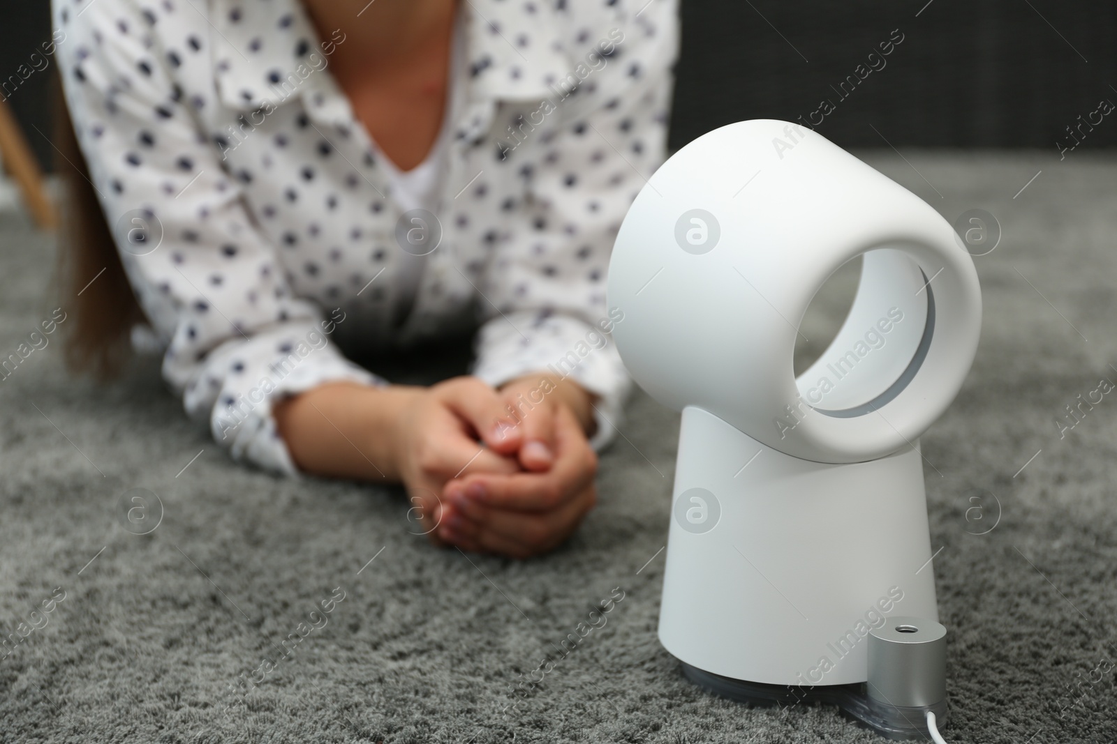 Photo of Woman lying in front of portable fan at home. Summer heat