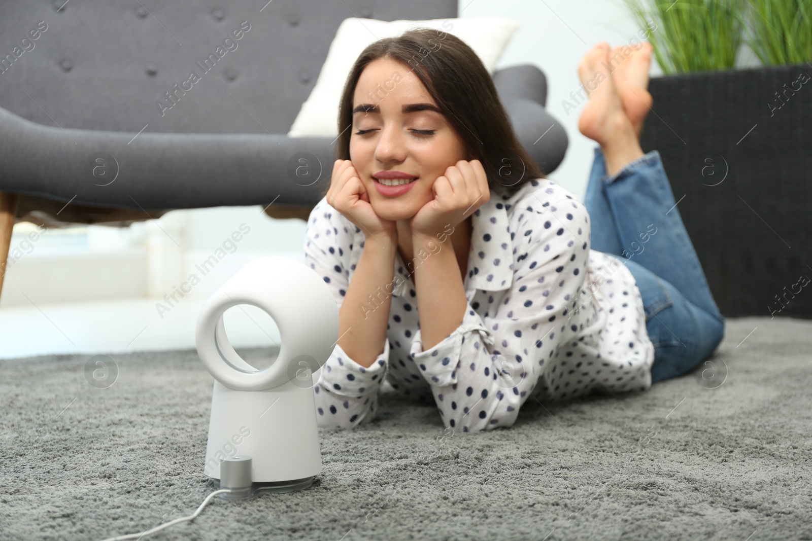 Photo of Woman enjoying air flow from portable fan at home. Summer heat