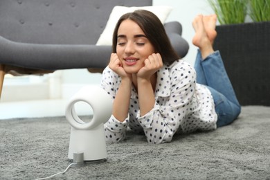 Photo of Woman enjoying air flow from portable fan at home. Summer heat
