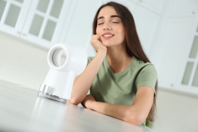 Photo of Woman enjoying air flow from portable fan in kitchen. Summer heat
