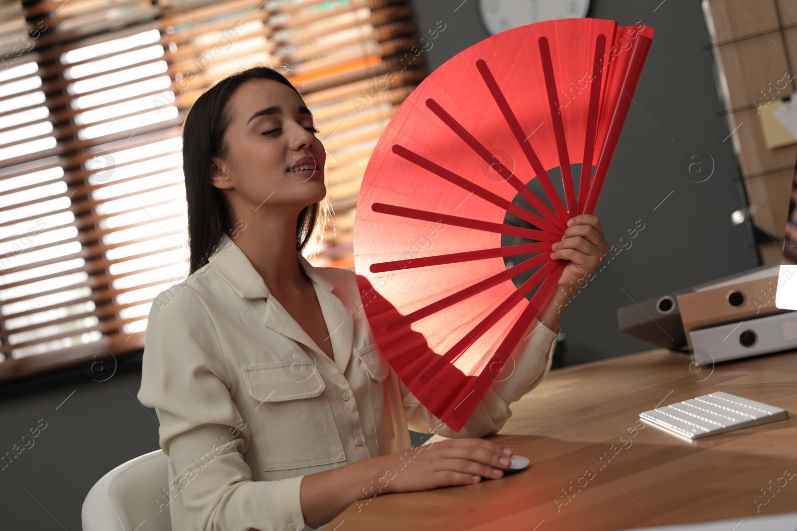 Photo of Woman enjoying air flow from hand fan at home. Summer heat
