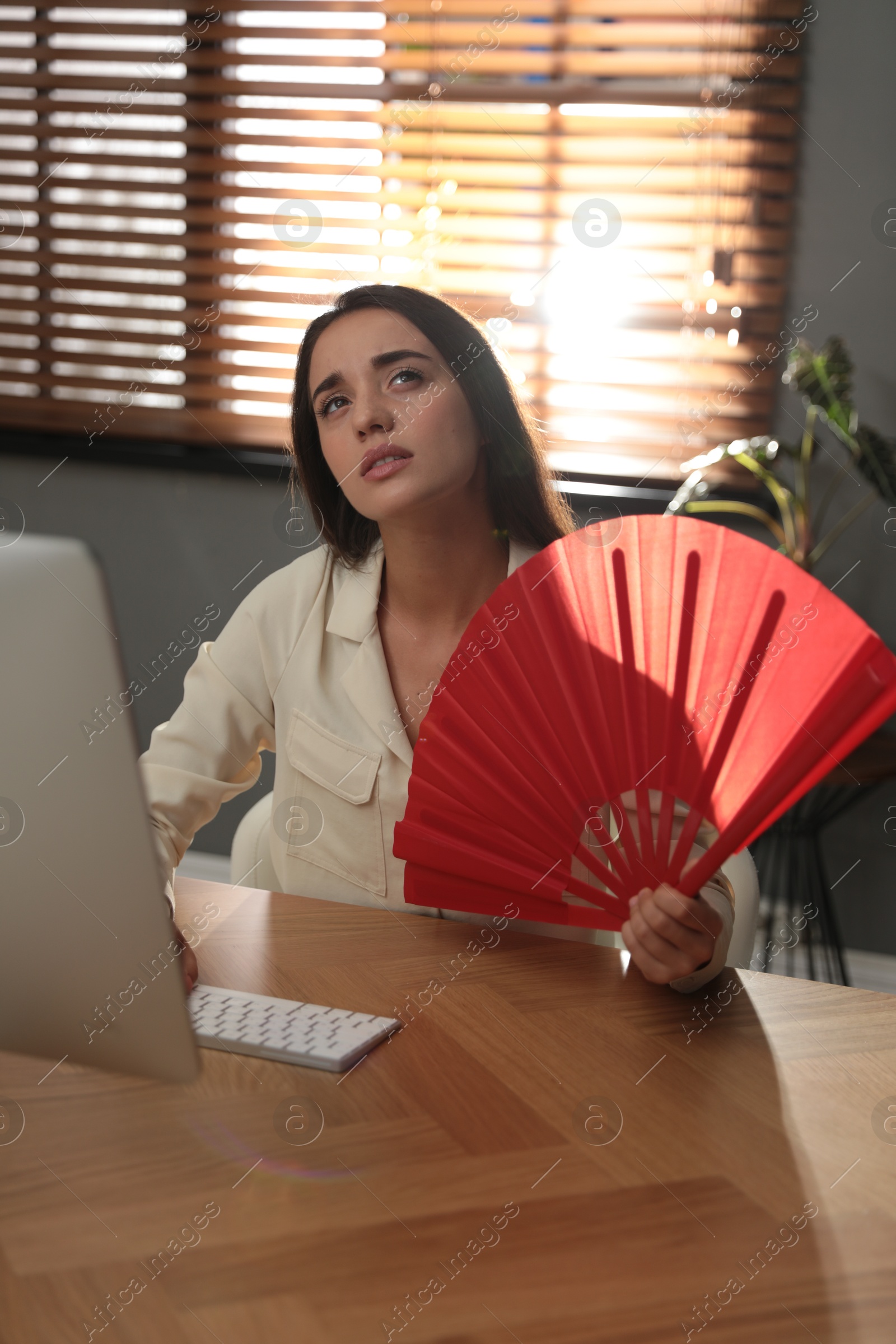 Photo of Woman with hand fan suffering from heat at home. Summer season