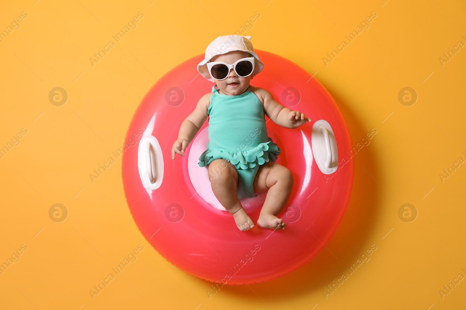 Photo of Cute little baby in sunglasses with inflatable ring on yellow background