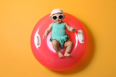 Photo of Cute little baby in sunglasses with inflatable ring on yellow background