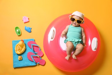 Photo of Cute little baby in sunglasses with inflatable ring and beach accessories on yellow background, top view