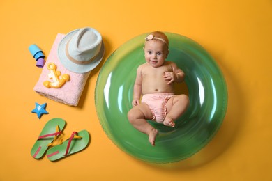 Photo of Cute little baby with inflatable ring and beach accessories on yellow background, top view