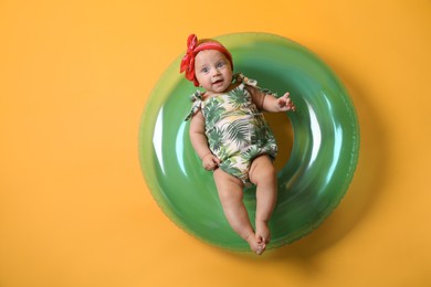 Photo of Cute little baby in headband with inflatable ring on yellow background