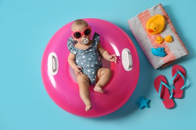 Photo of Cute little baby in sunglasses with inflatable ring and beach accessories on light blue background, top view