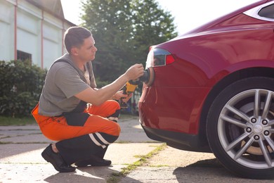 Photo of Man polishing car with orbital polisher outdoors