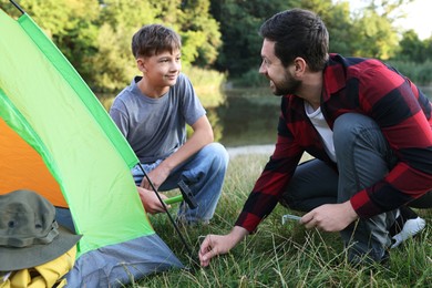 Photo of Father and son setting up camping tent near river outdoors