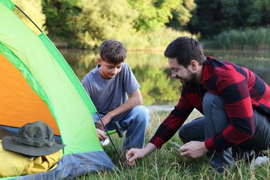 Photo of Father and son setting up camping tent near river outdoors