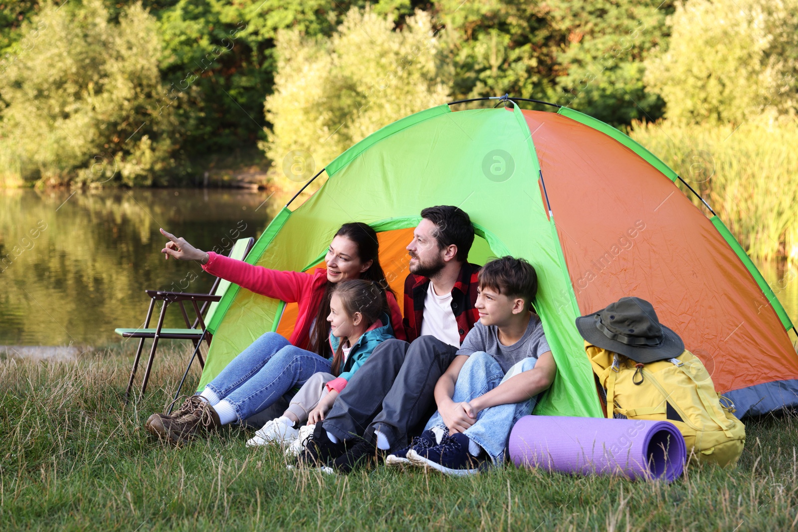 Photo of Happy family spending time together with camping tent and tourist equipment near river outdoors