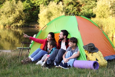 Photo of Happy family spending time together with camping tent and tourist equipment near river outdoors