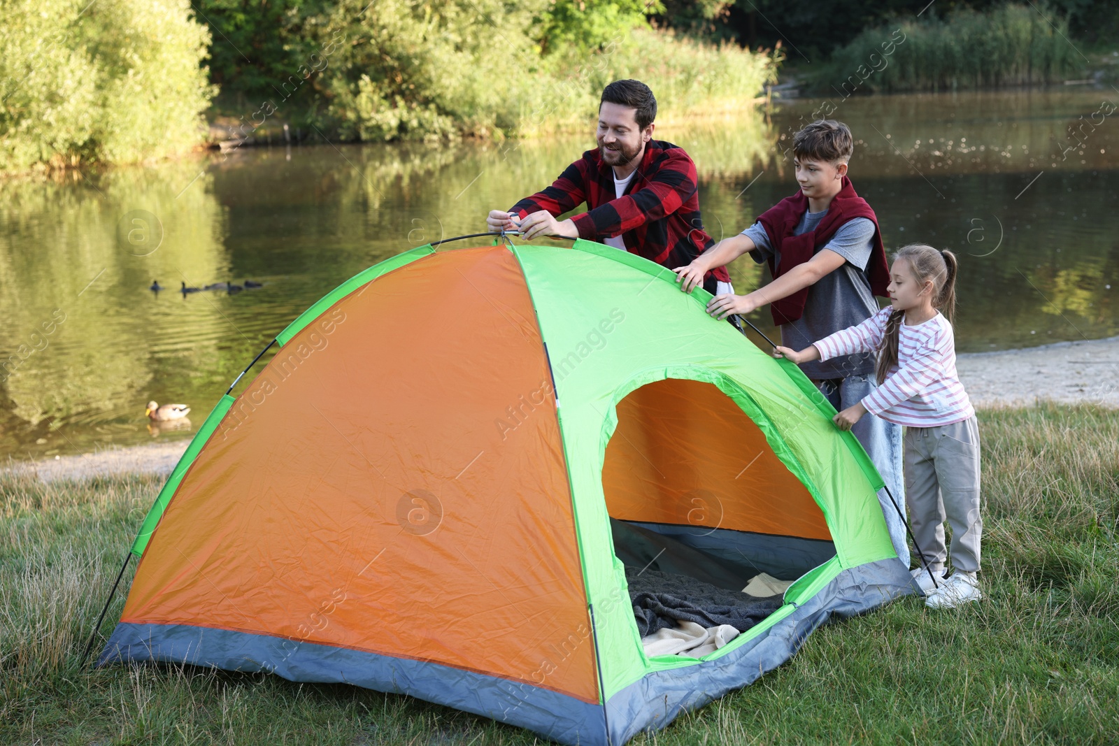 Photo of Happy father and his children setting up camping tent near river outdoors