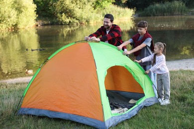 Photo of Happy father and his children setting up camping tent near river outdoors